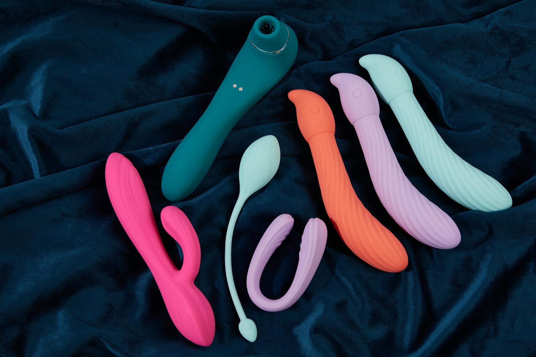 Vibrant collection of silicone clitoral vibrators on blue fabric, showing various shapes and colors for sexual wellness.