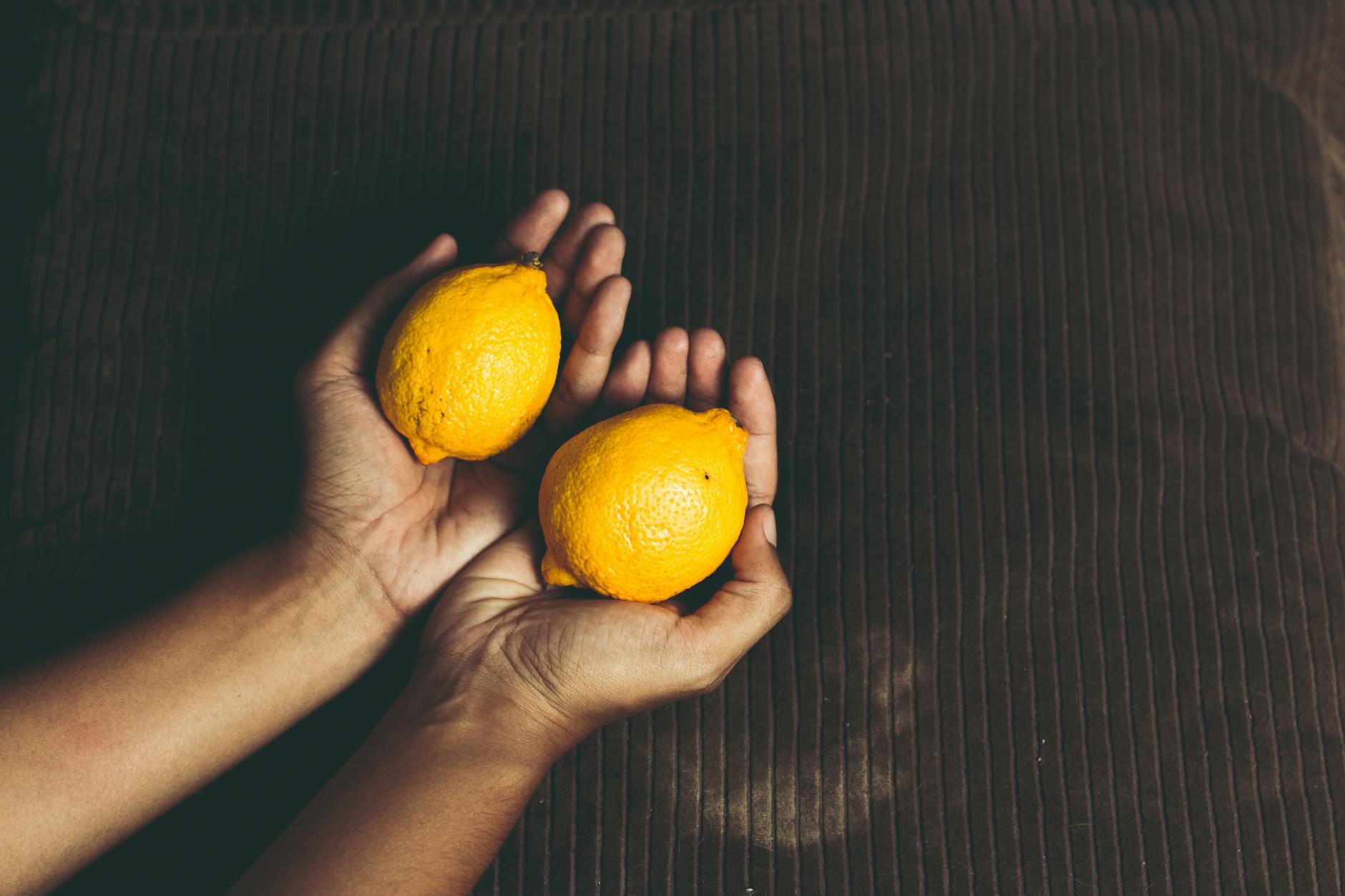 Two fresh lemons held in cupped hands on a brown surface, symbolizing the subtle shifts in sensation and pleasure