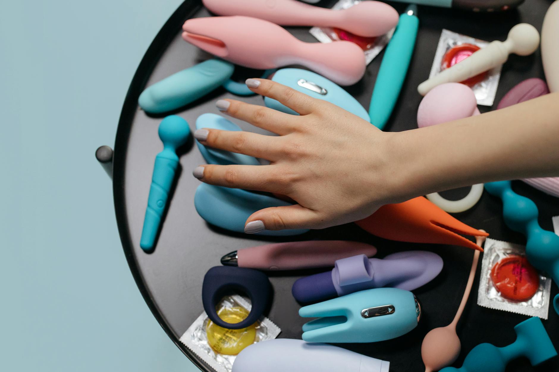 Hands exploring a range of colorful vibrators on a table, representing options and choice in sexual wellness.