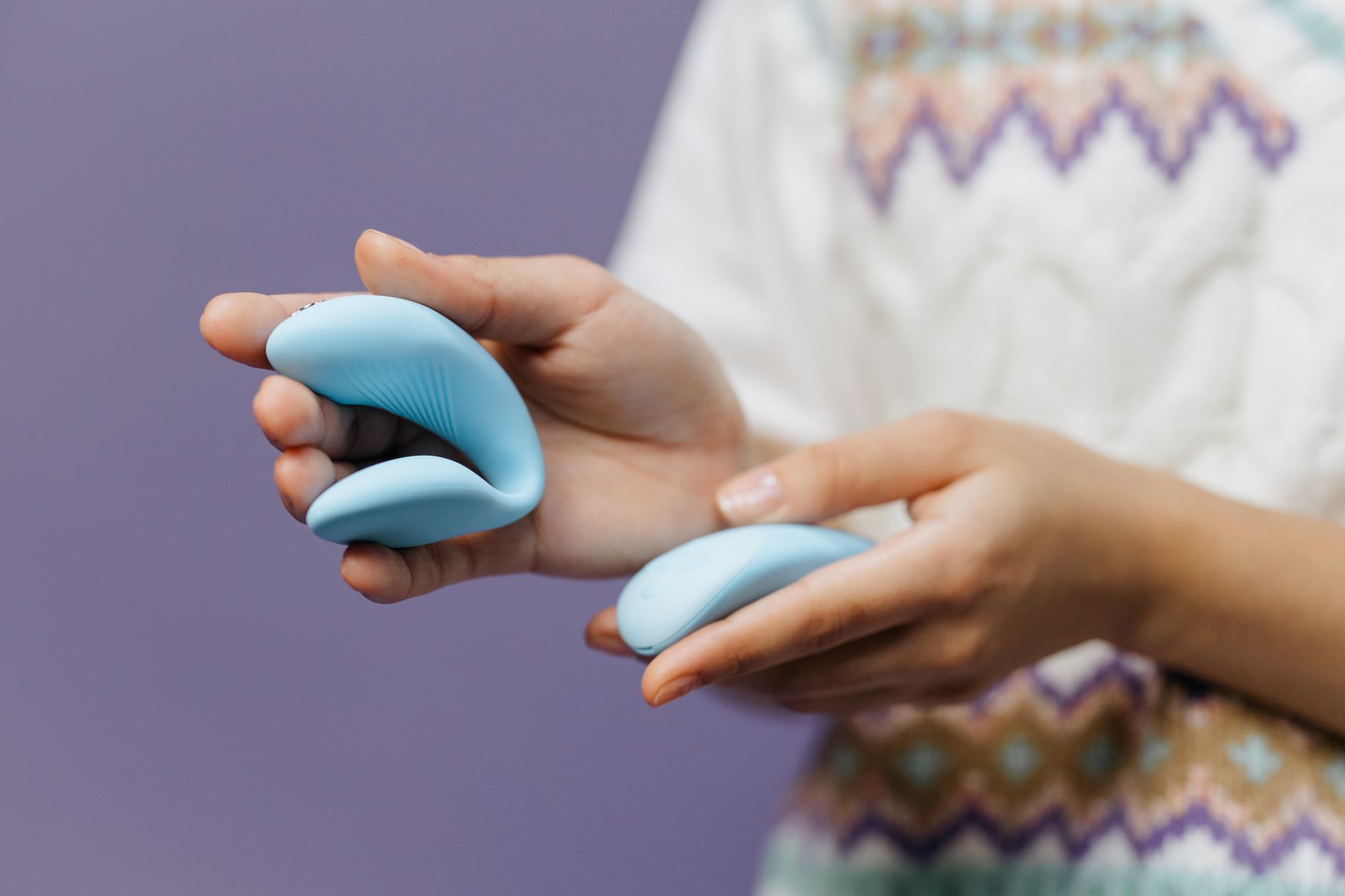 A sleek lemon clitoral vibrator held in hands against a purple background.