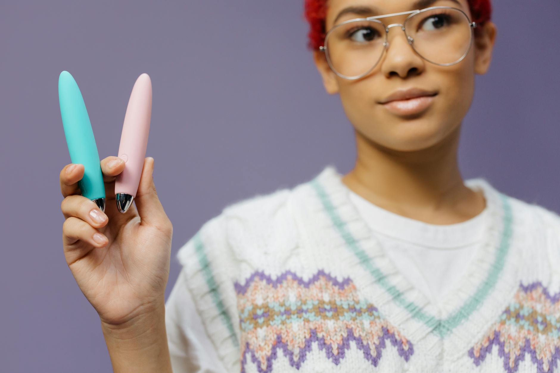 Woman holding two different vibrator styles against a purple background
