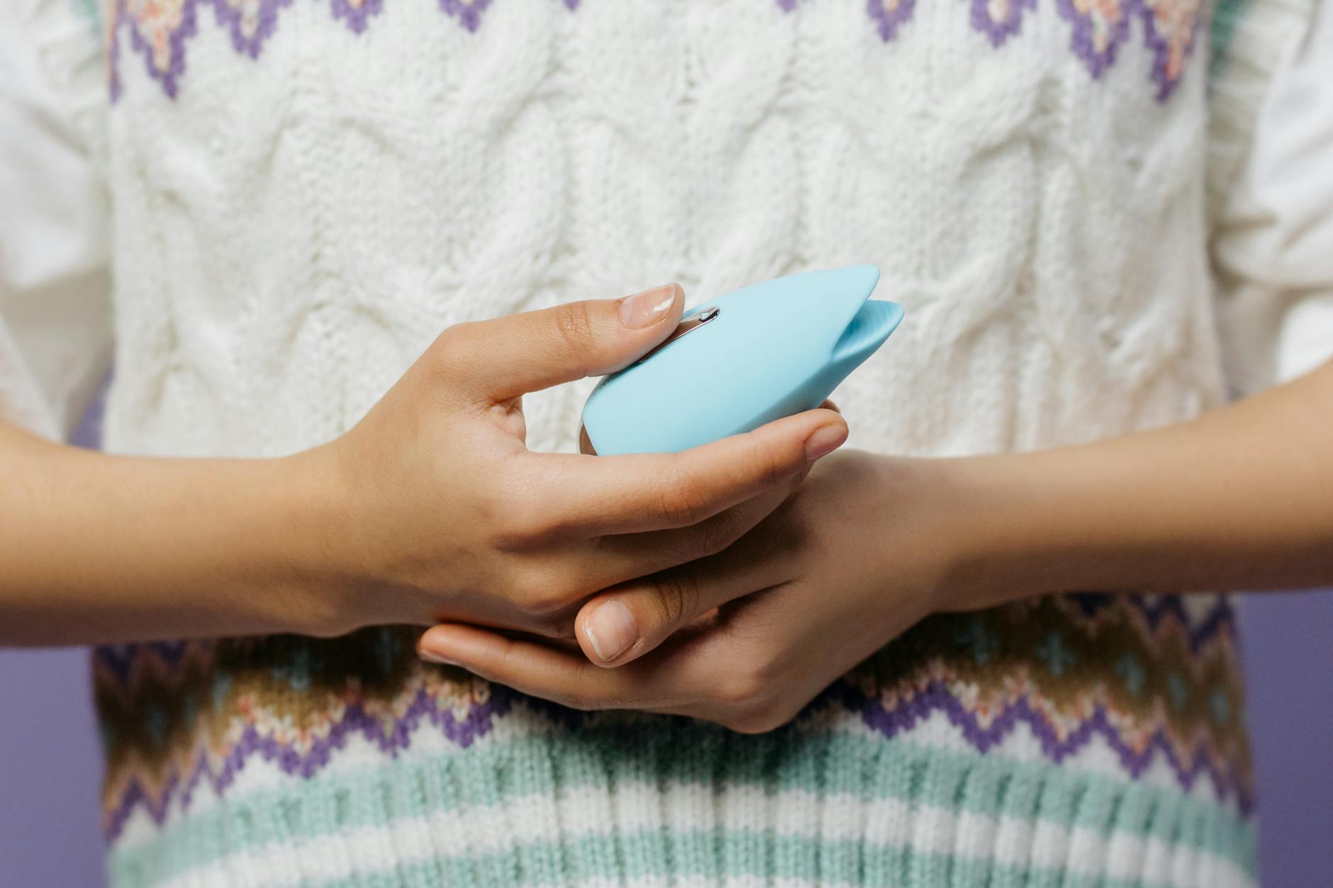 Mulher segurando vibrador azul contra suéter de tricô, explorando o prazer com segurança após recuperação de saúde